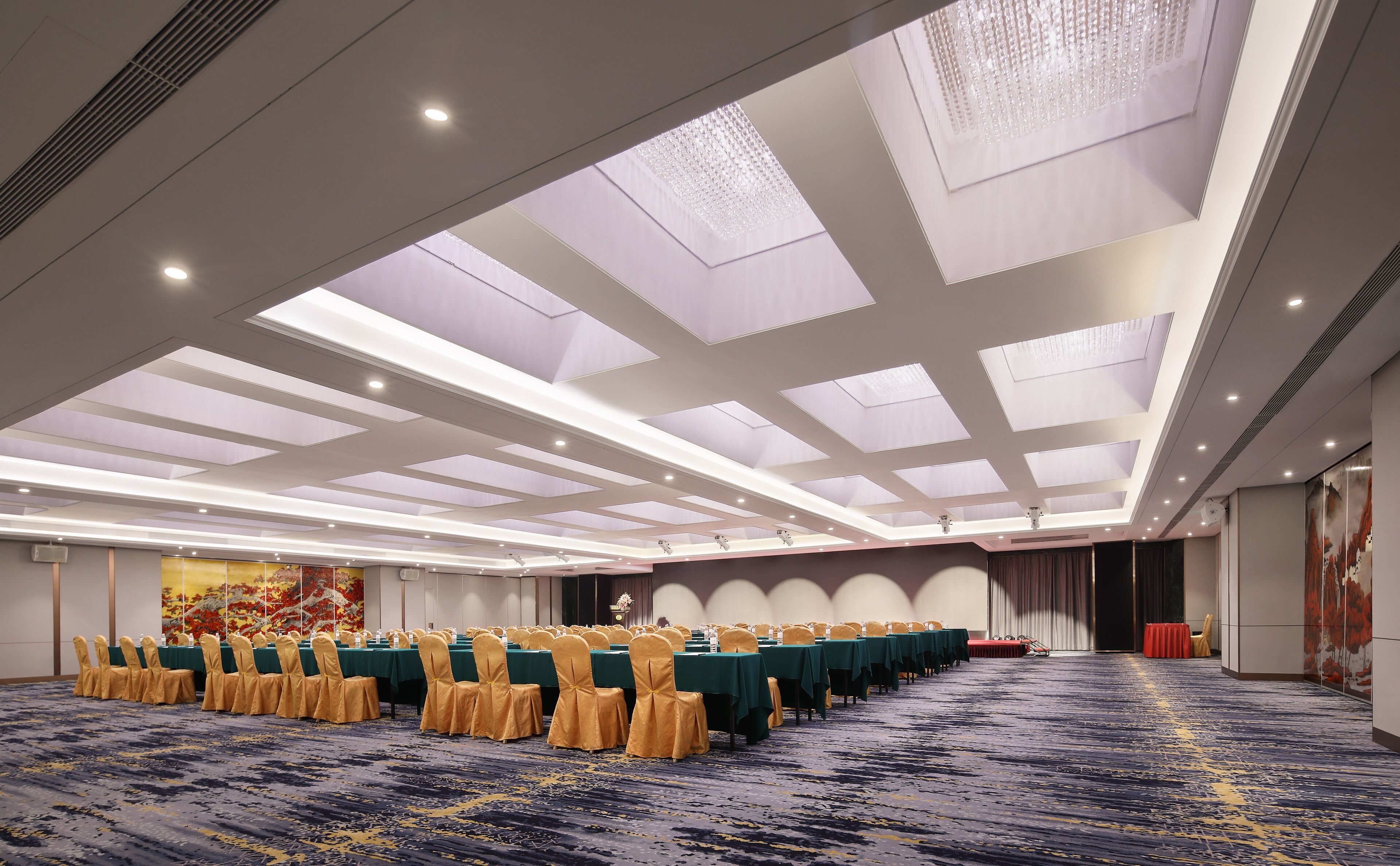 A large conference room with tables and chairs, a patterned carpet, and a high ceiling with skylights.