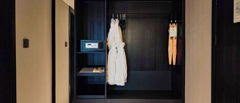 Ein Hotelzimmer mit einem dunklen Holzschrank, einem an der Tür hängenden Bademantel und einem kleinen Regal mit einem Radio und einem Buch.