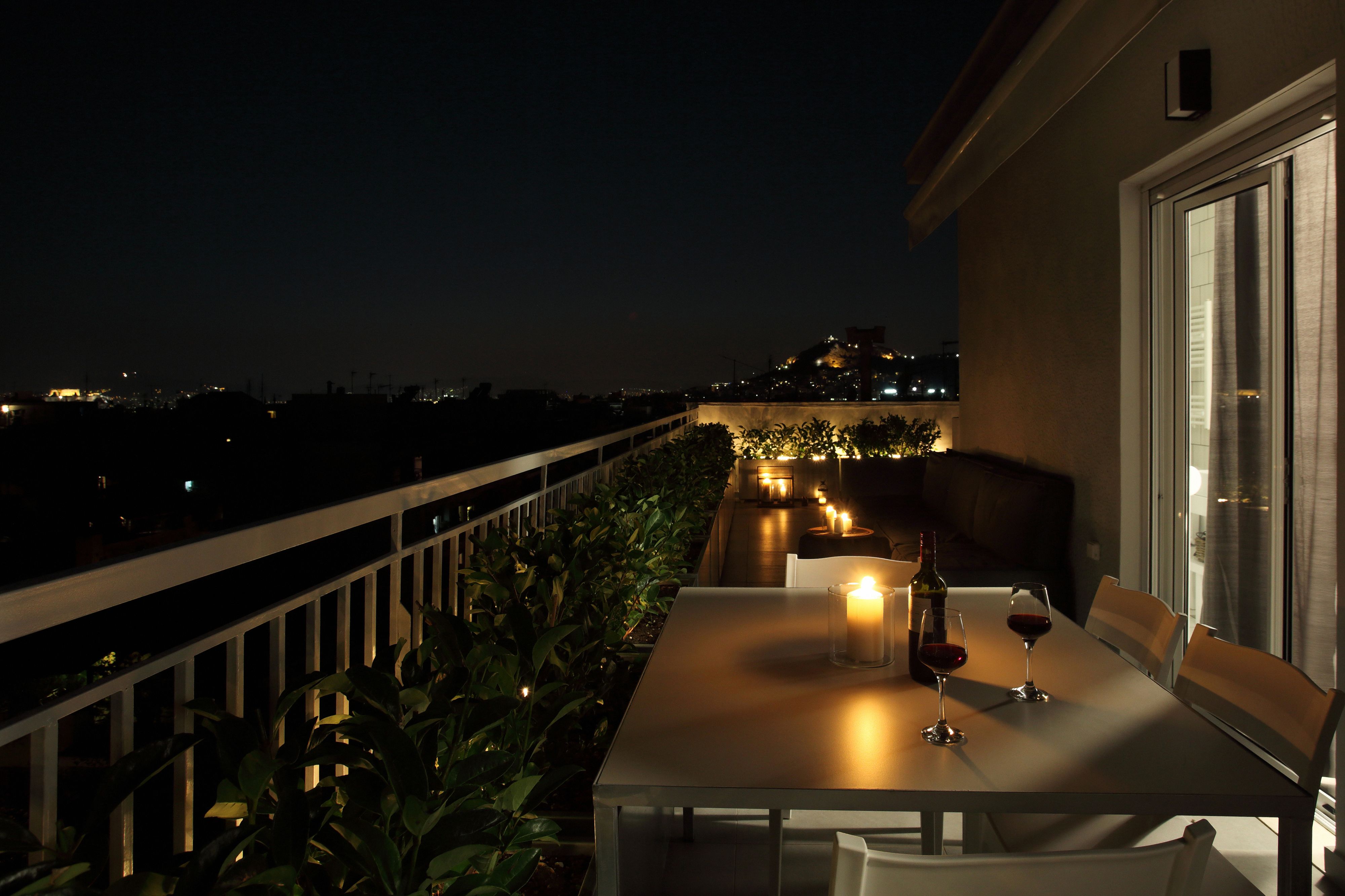 A balcony with a table set for two, candles, and wine glasses.