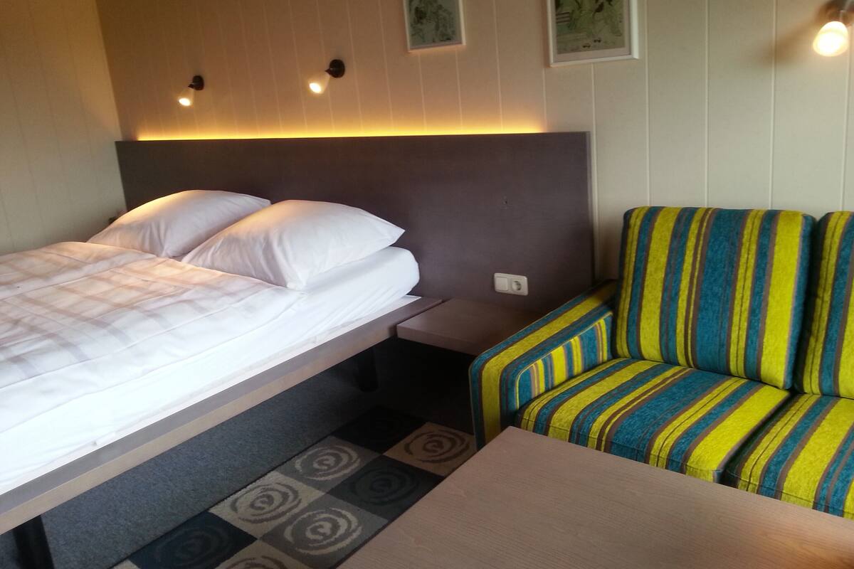 A hotel room with a bed, a small table, and a striped sofa.