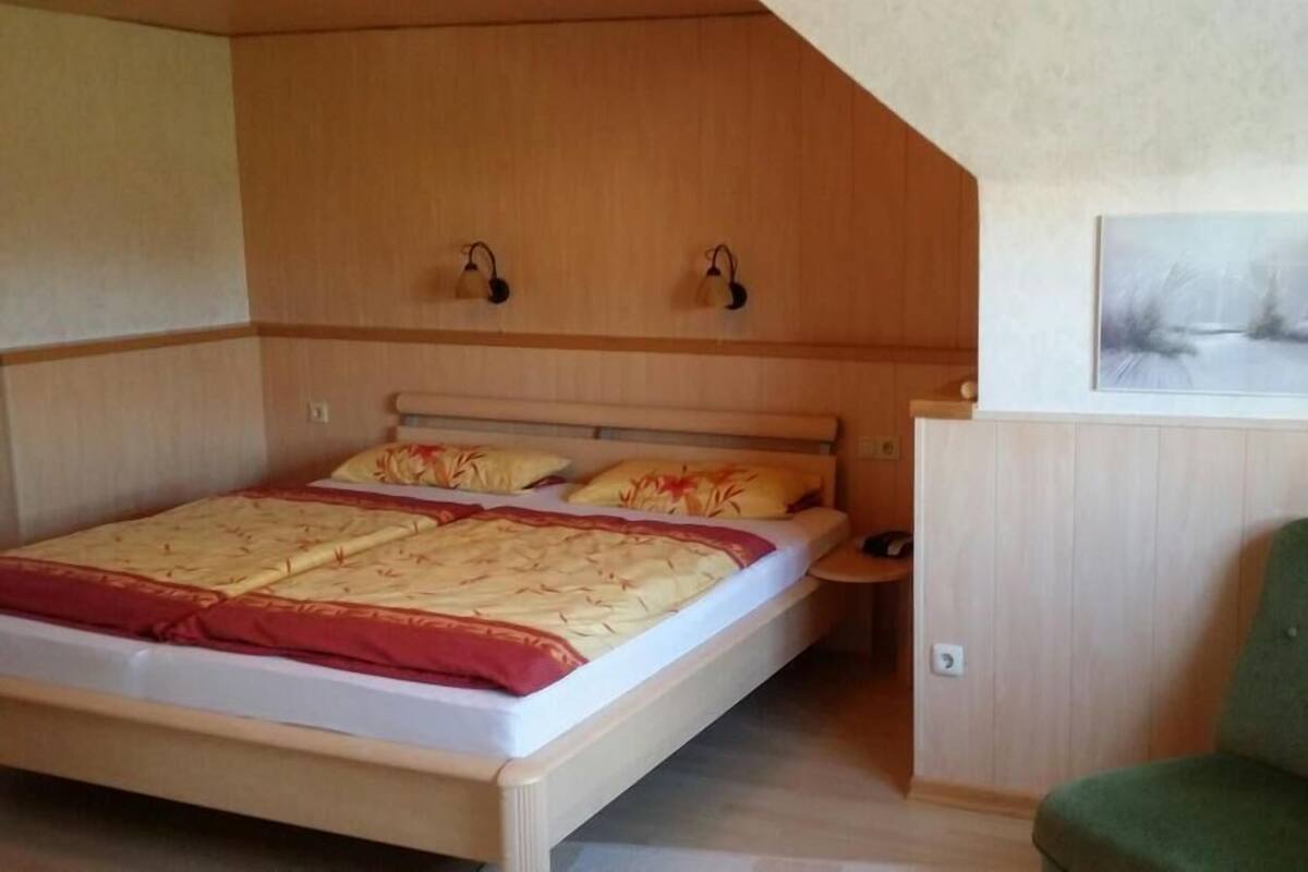 A bedroom with a wooden bed, a green chair, and a painting on the wall.