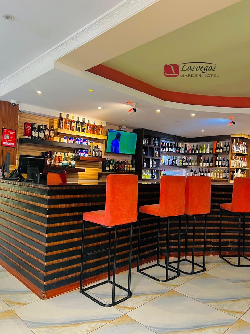 A bar area with a counter, multiple liquor bottles, a television screen, and bar stools.