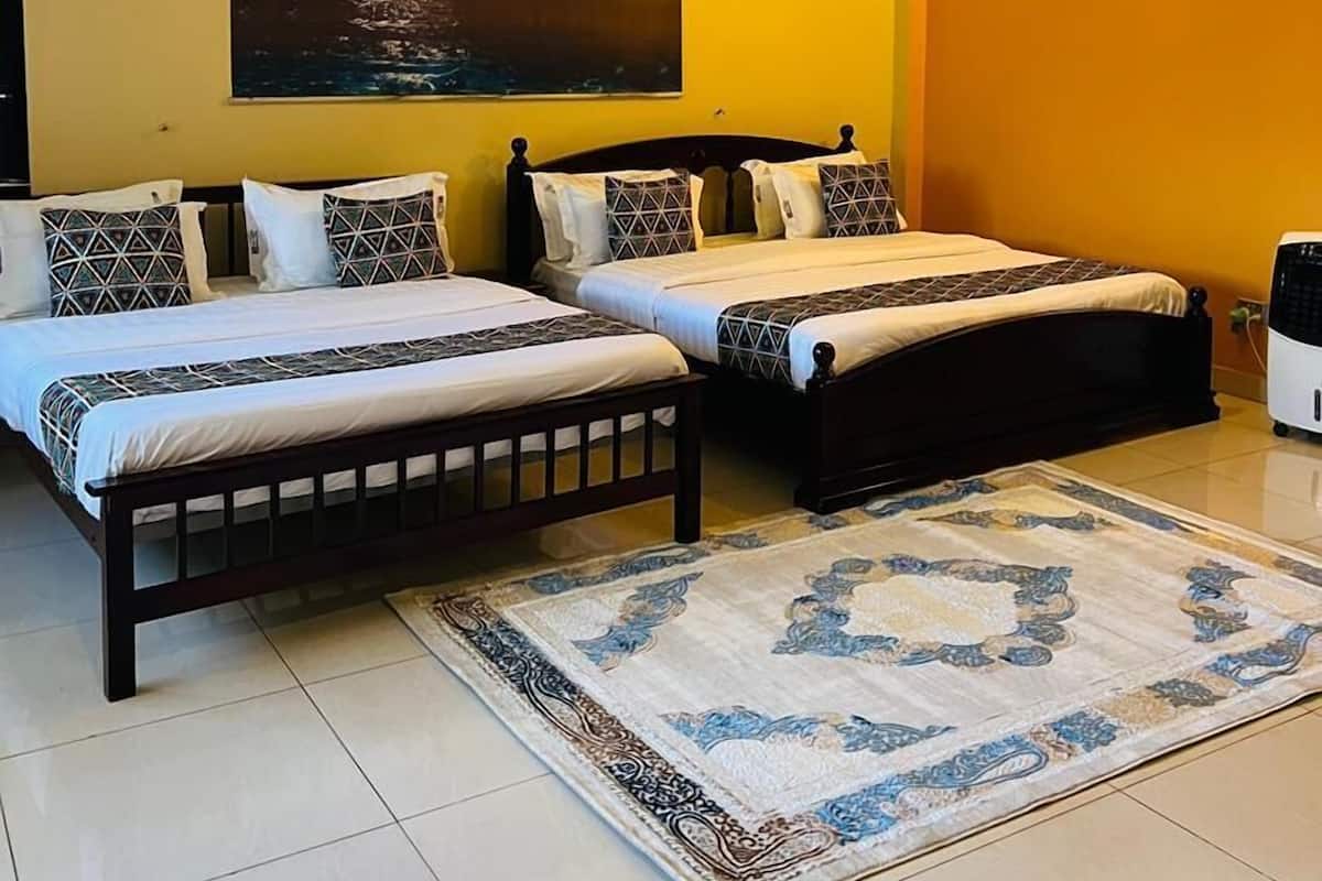 A hotel room with two beds, a large painting of a moonlit night, a rug, and a heater.