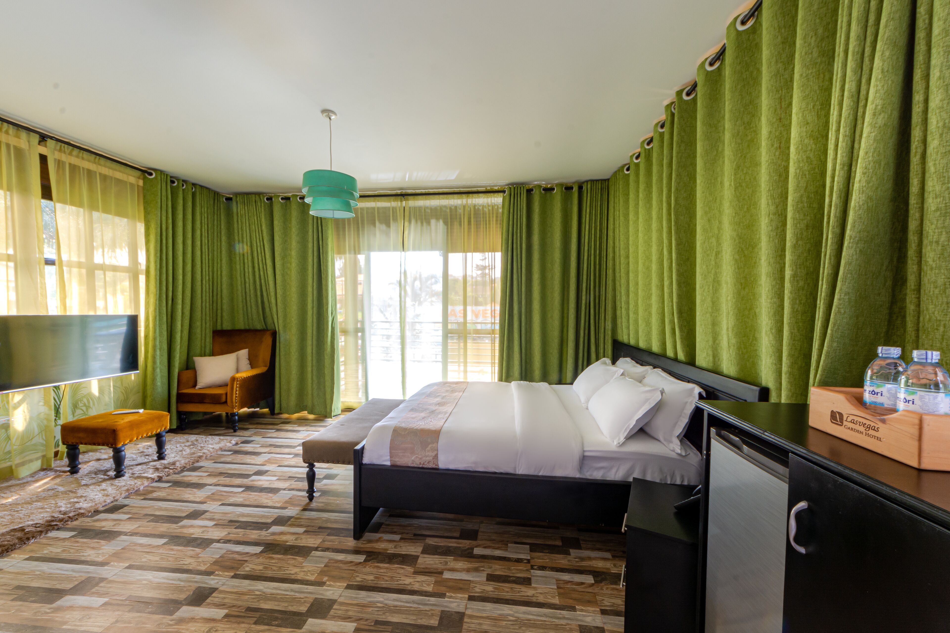Habitació d'hotel amb un llit, una televisió, una banca de fusta i un escriptori amb una ampolla d'aigua.