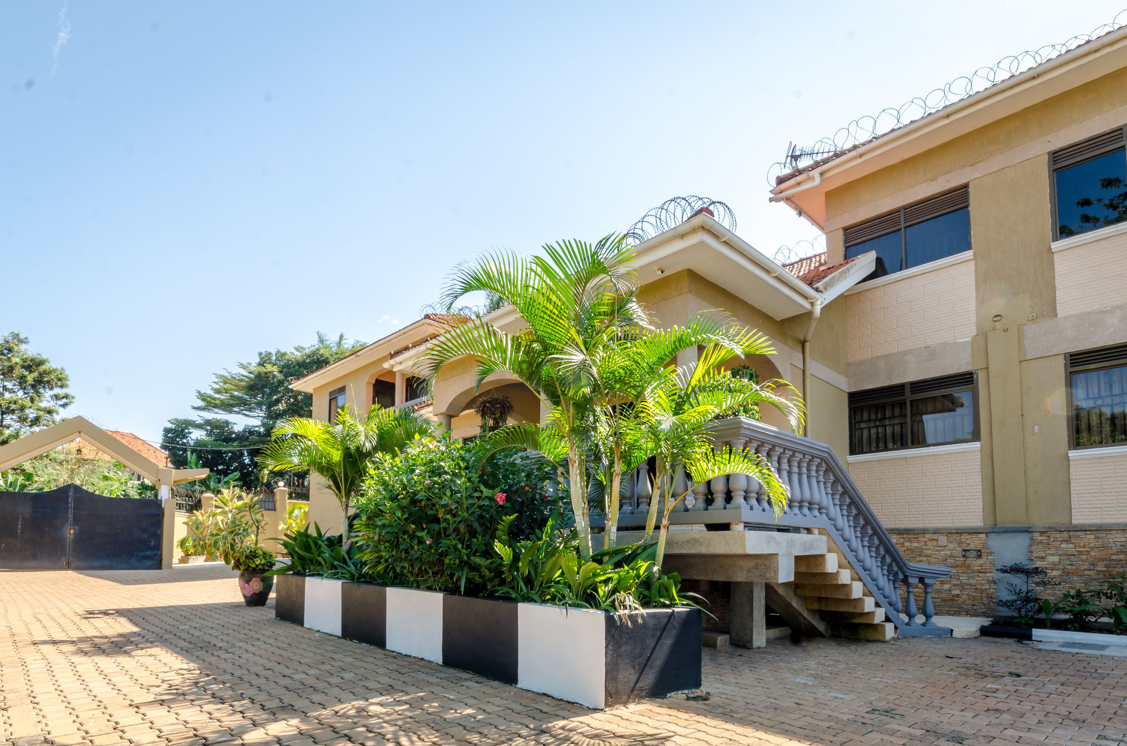 Uma casa de dois andares com portão, escadaria e um jardim bem cuidado com diversas plantas.