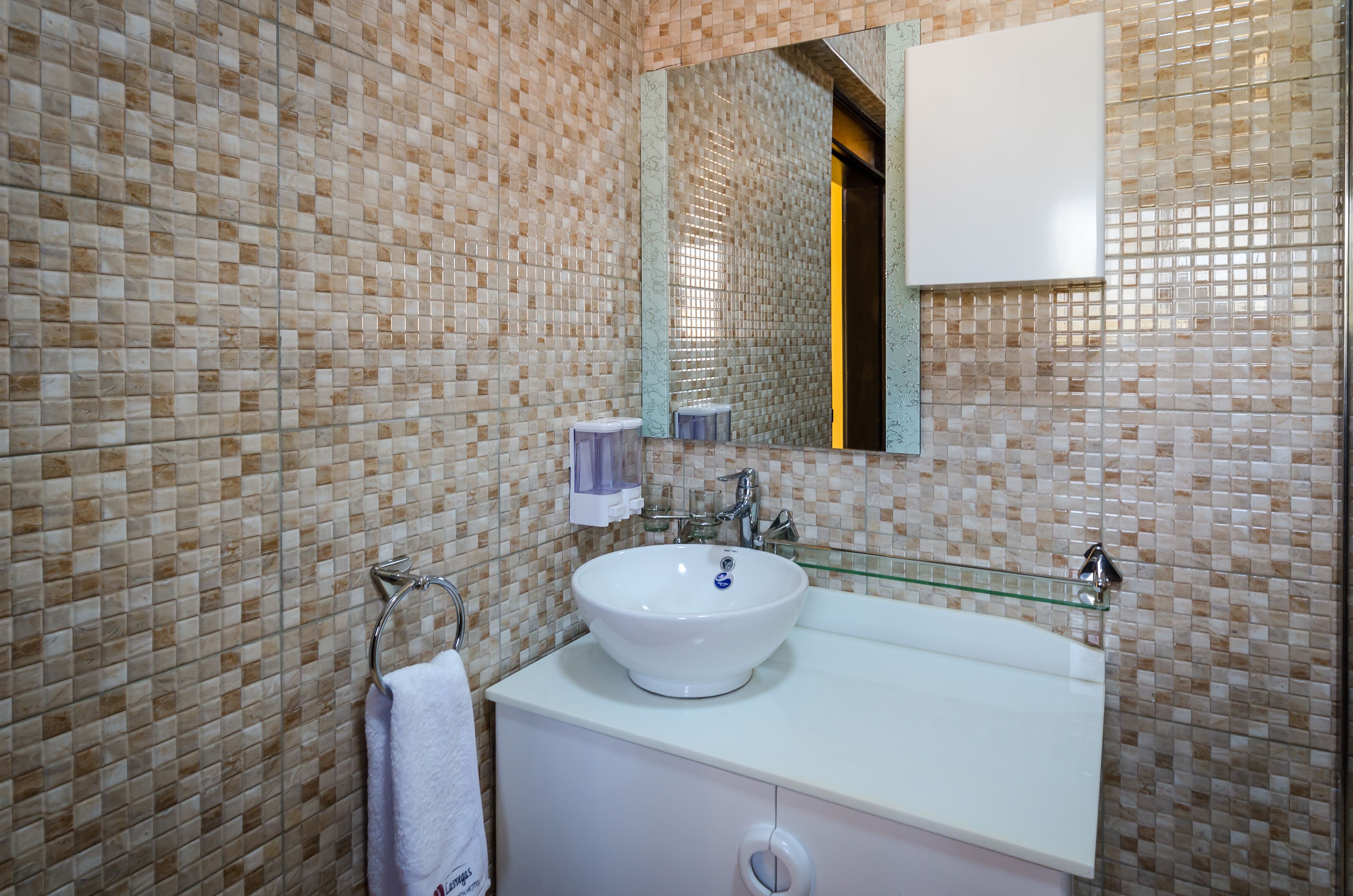 Un baño con un lavamanos blanco, un estante de vidrio y un espejo encima.