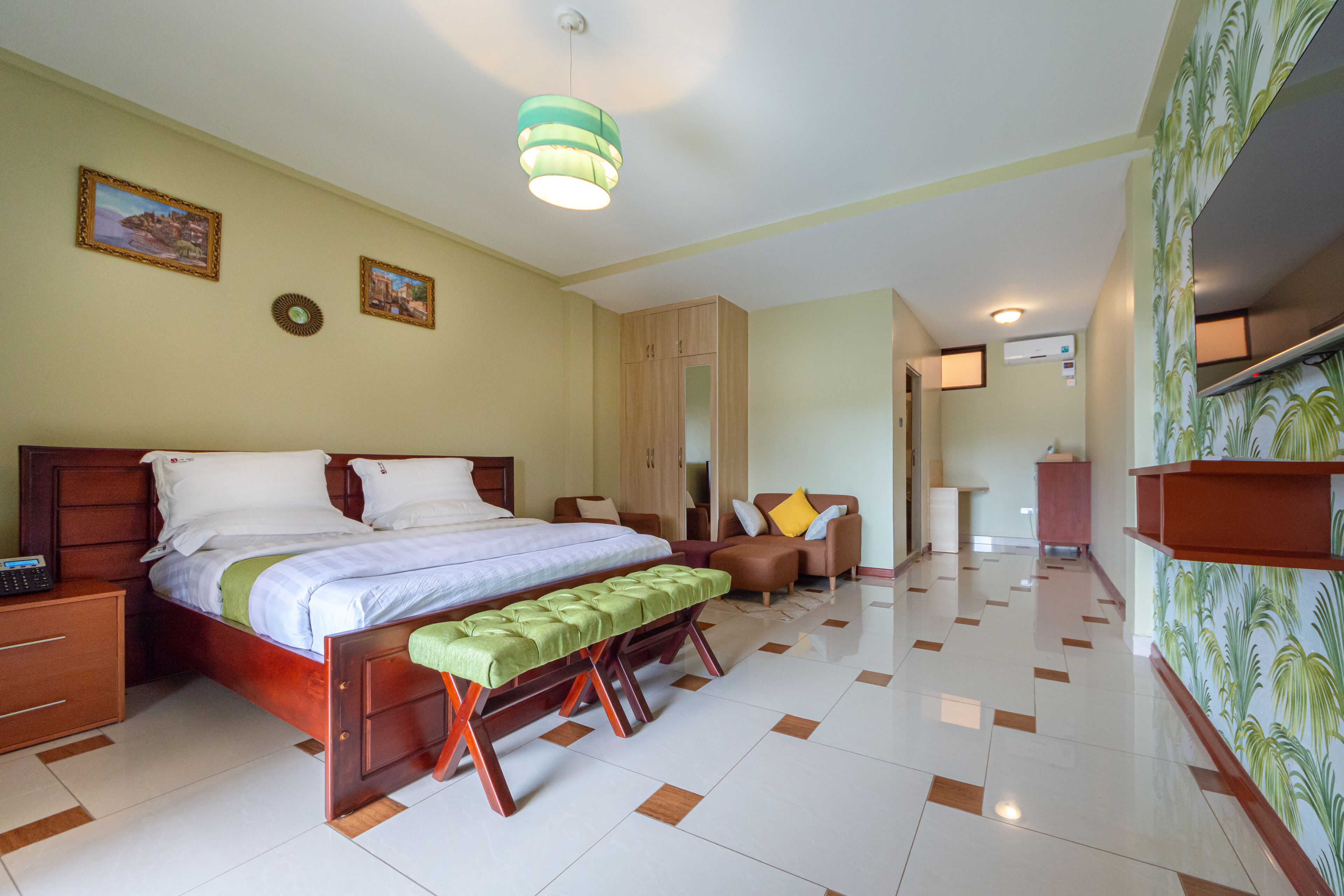 A hotel room with a large bed, a bench, a desk, and a wardrobe.