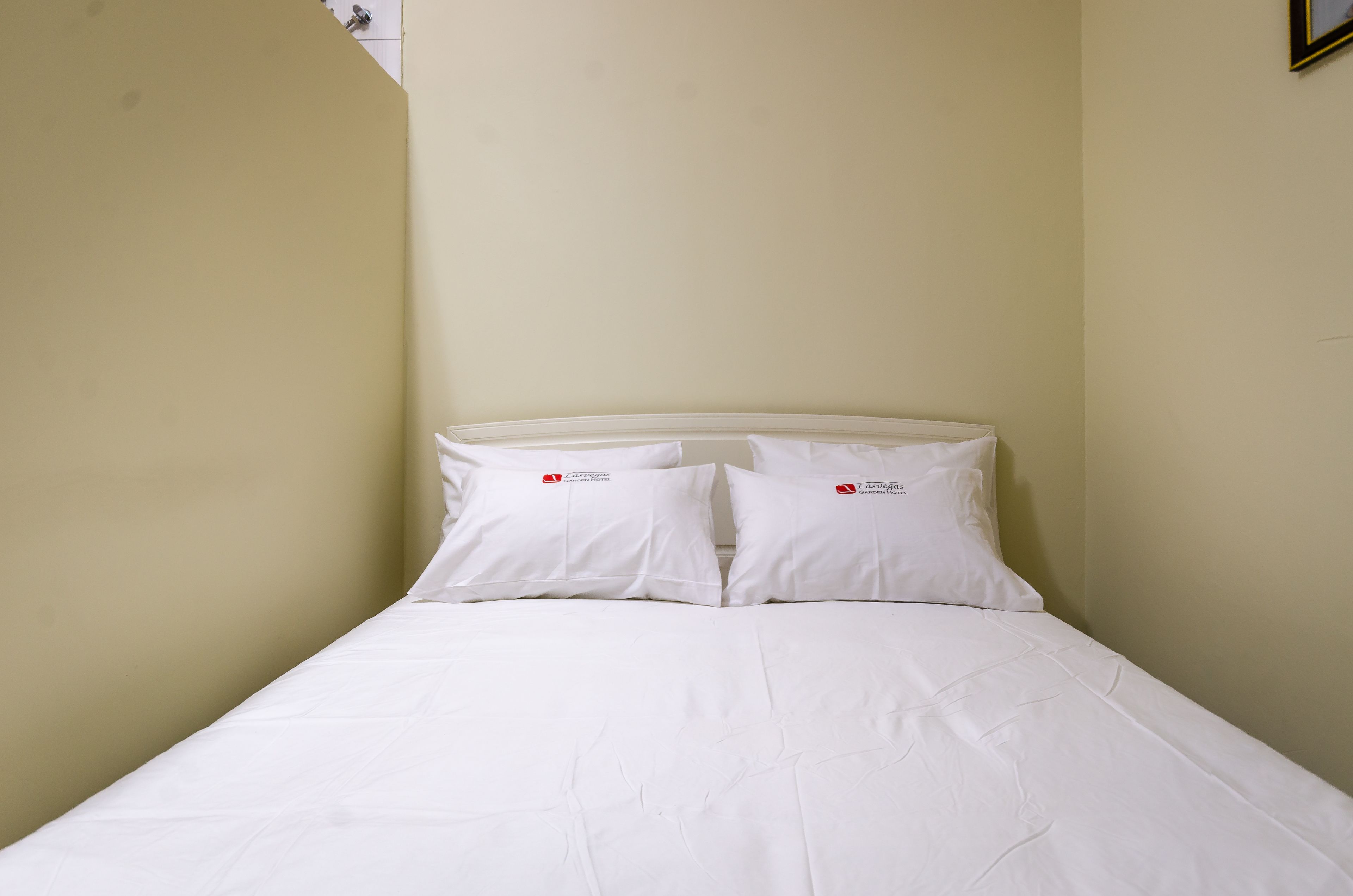 Una cama individual con ropa de cama y almohadas blancas, una pared lisa y un ventanal con vistas al cielo.