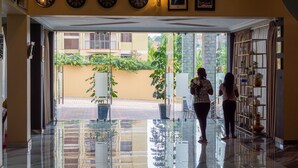 Um saguão de hotel com entrada de vidro, relógios mostrando diferentes horários de cidades e vista para a área externa.