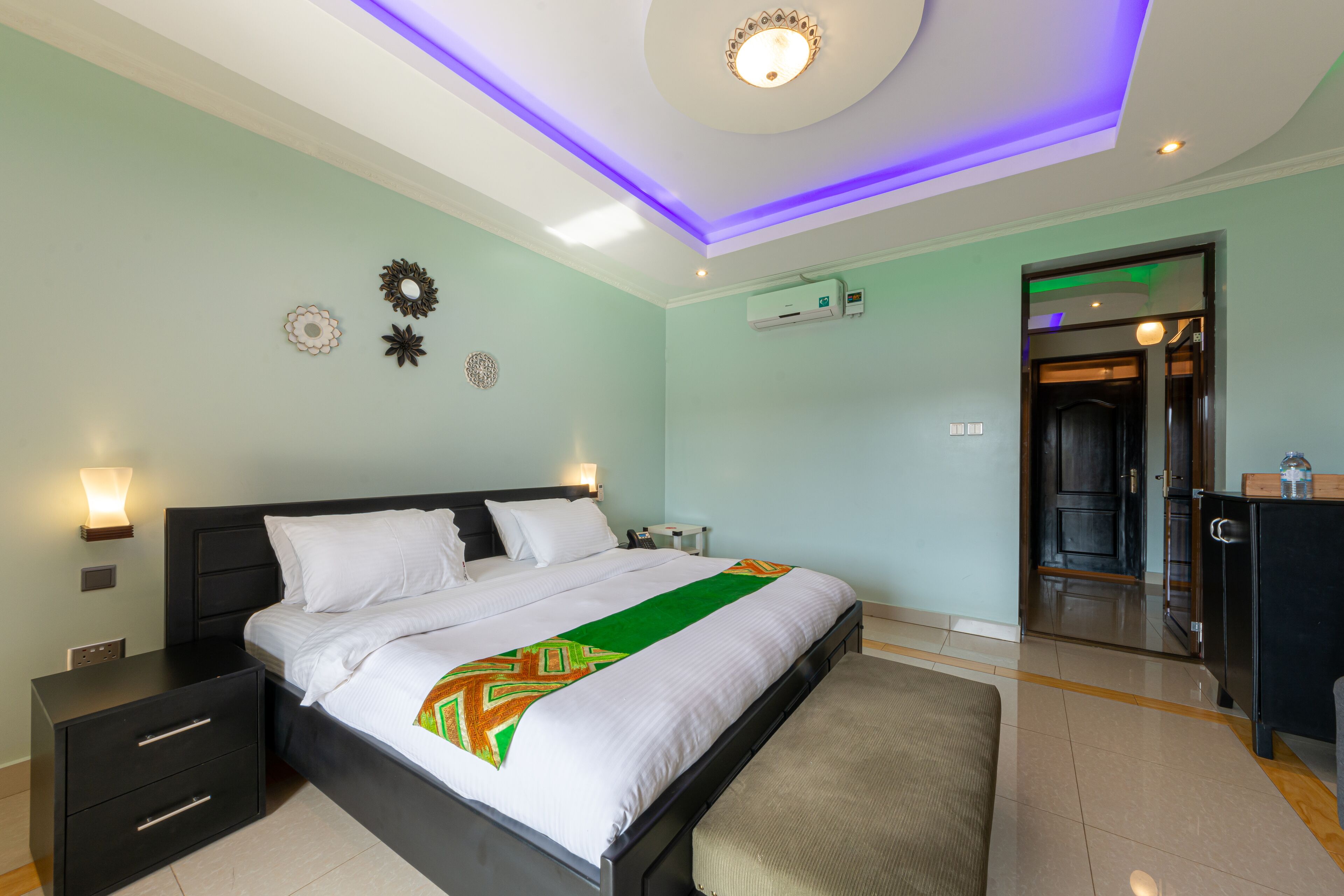 A modern bedroom with a bed, bedside tables, a bench, and a door leading to a bathroom.