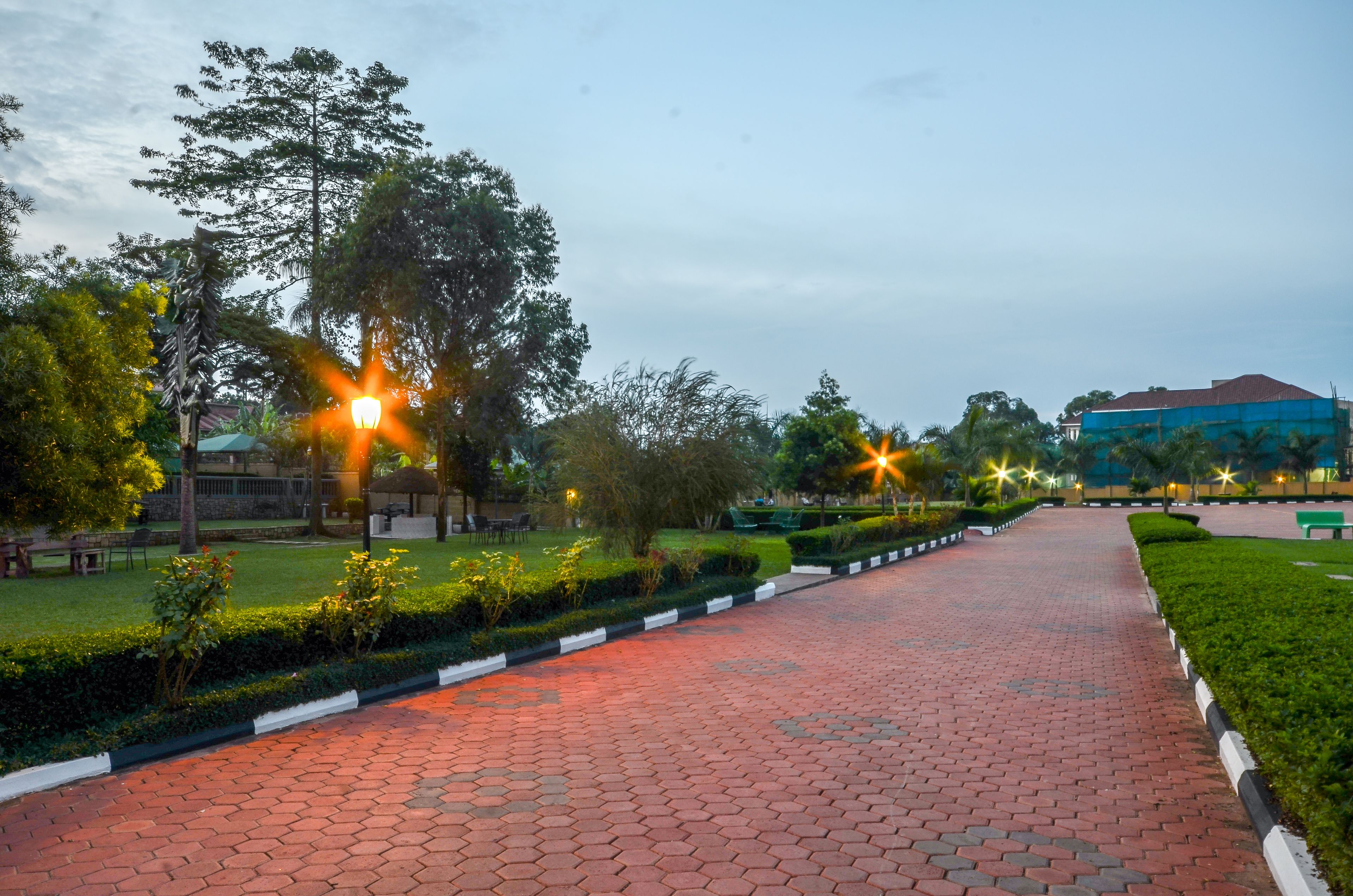 A paved pathway lined with trees and benches, leading to a building with a blue roof.
