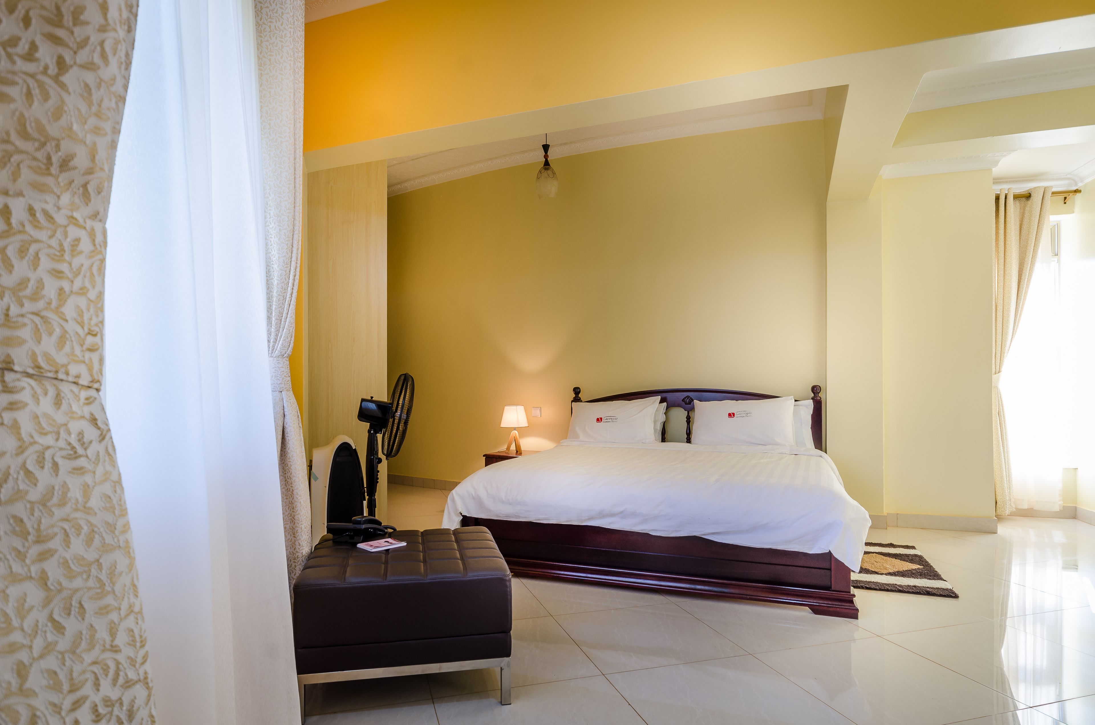 Una habitación de hotel con una cama grande, una mesita de noche, una lámpara y una ventana con cortinas.