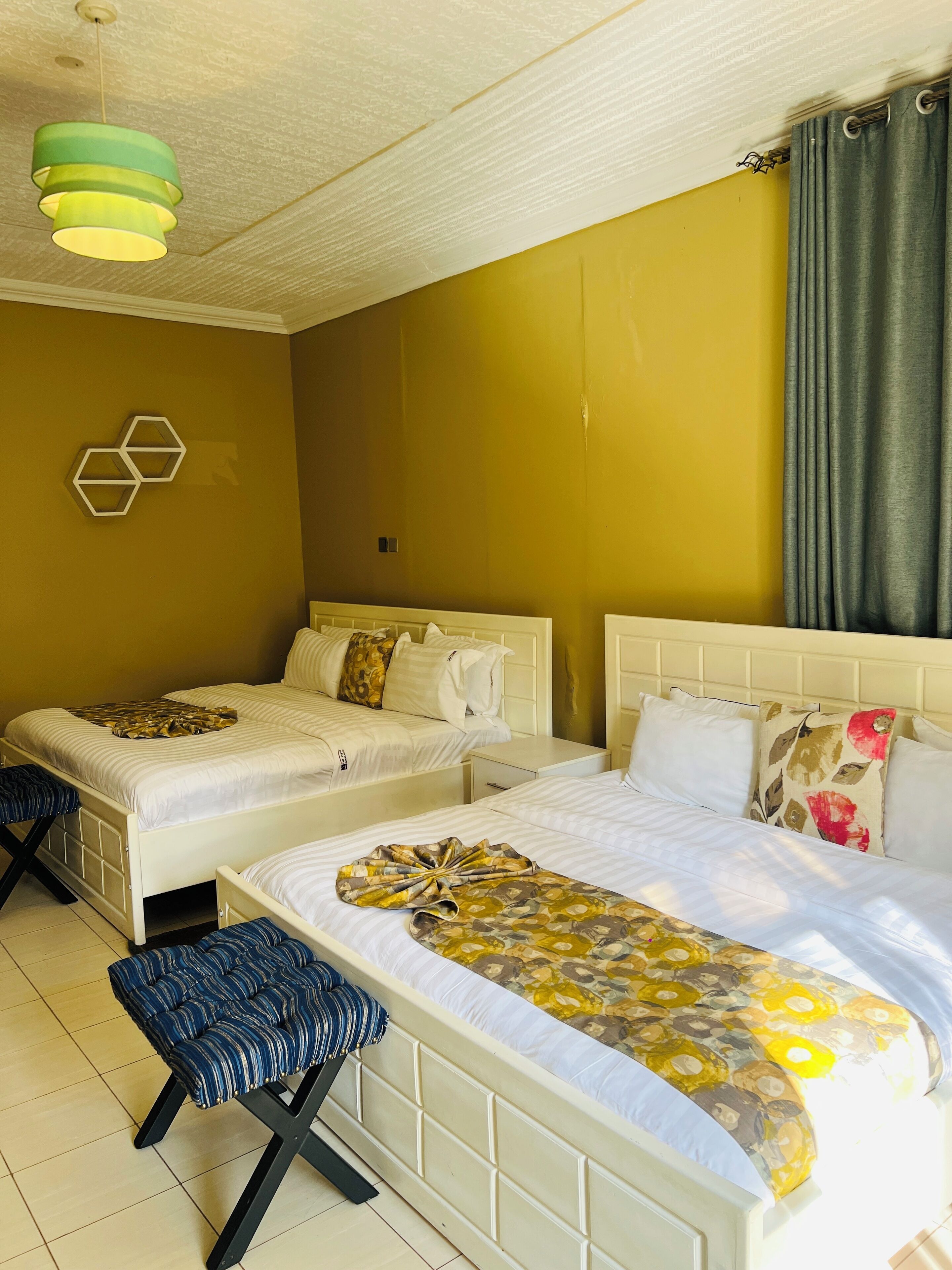 A hotel room with two beds, a bench, a hanging light fixture, and a wall-mounted hexagonal decoration.