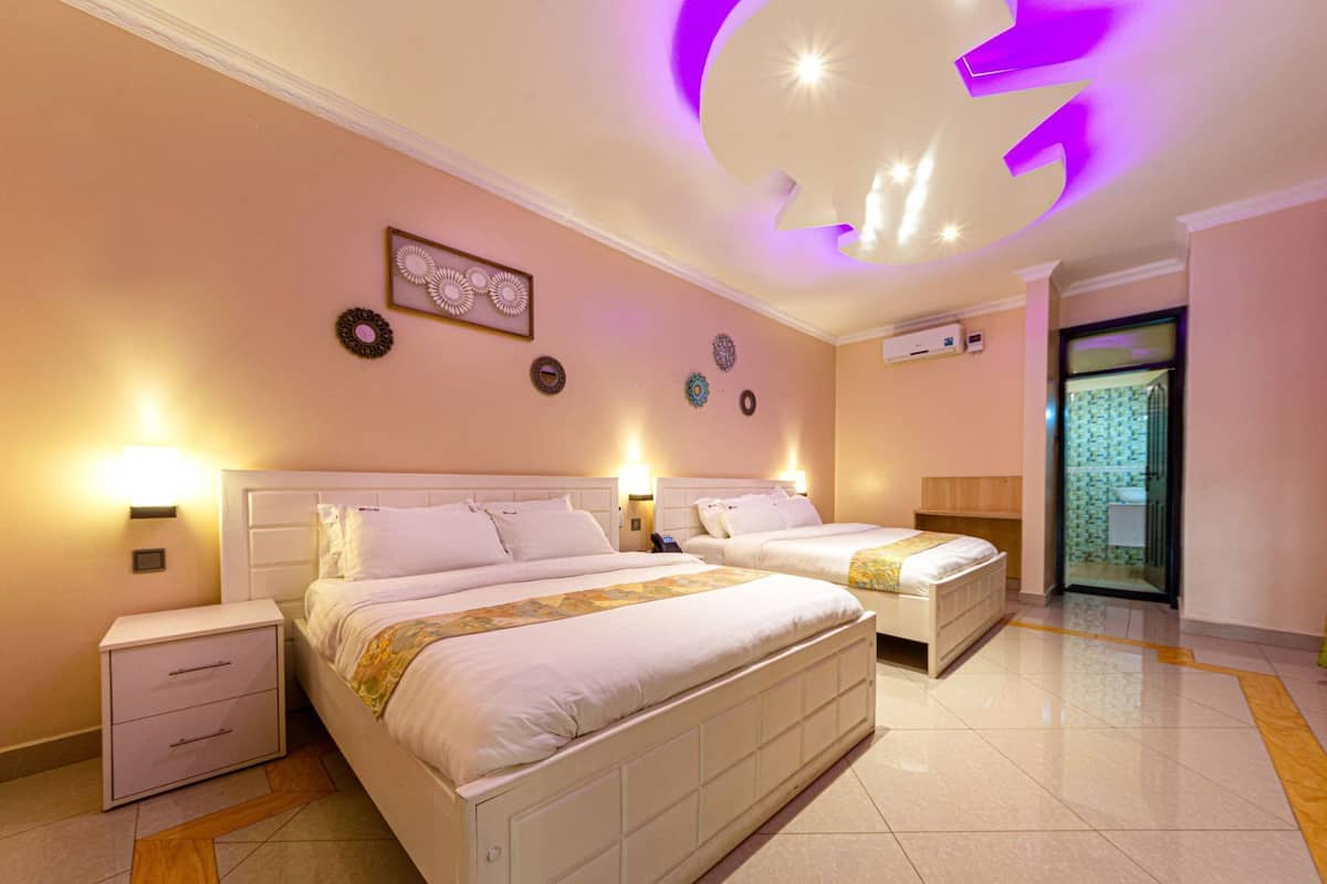 A hotel room with two beds, a nightstand, a wall-mounted lamp, a ceiling light, and a bathroom door.