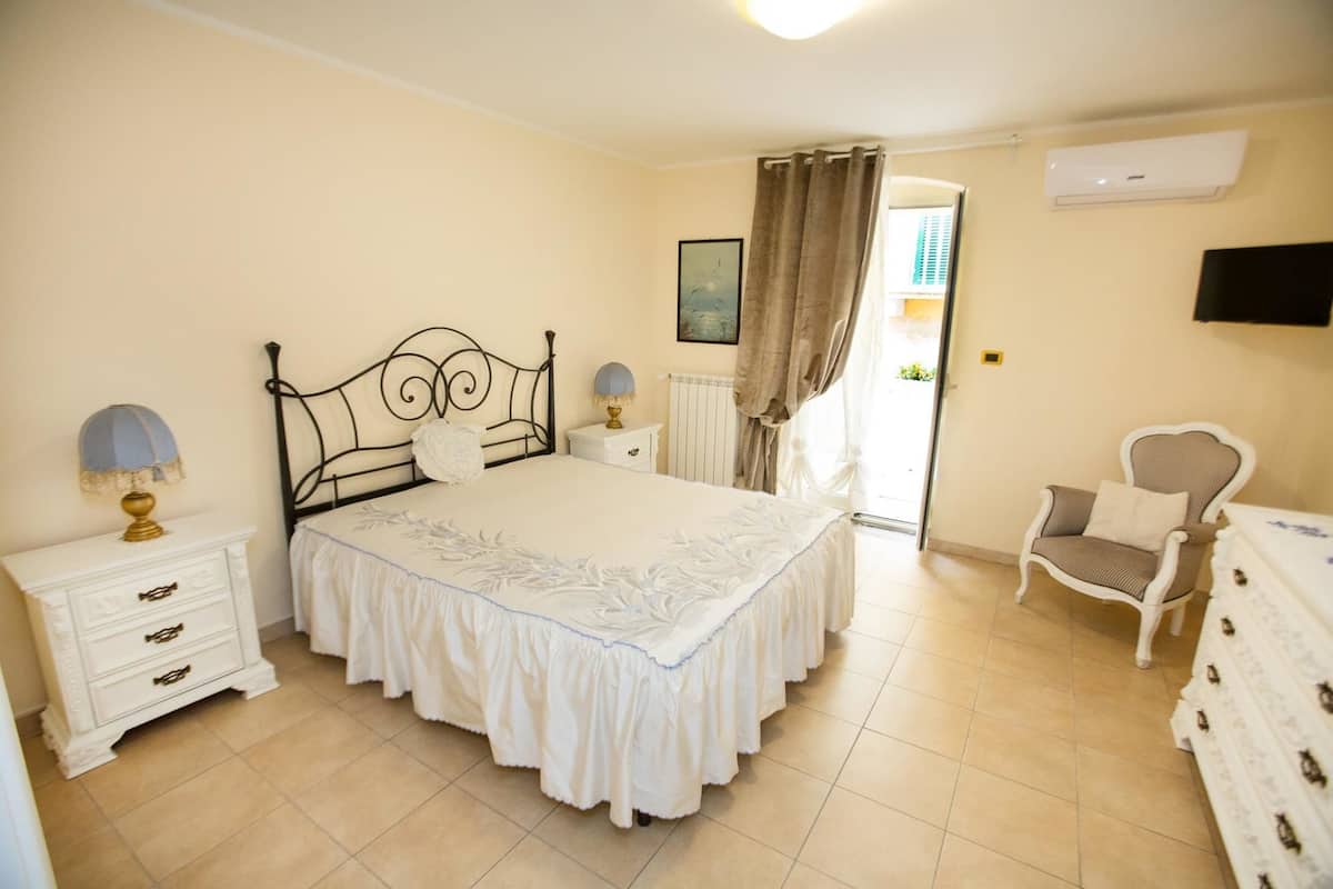 A bedroom with a large bed, bedside tables, a chair, a dresser, and a TV mounted on the wall.