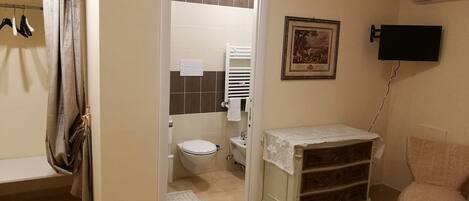 A bathroom with a toilet, a sink, a mirror, and a shower. There is a towel rack with towels and a shower curtain.