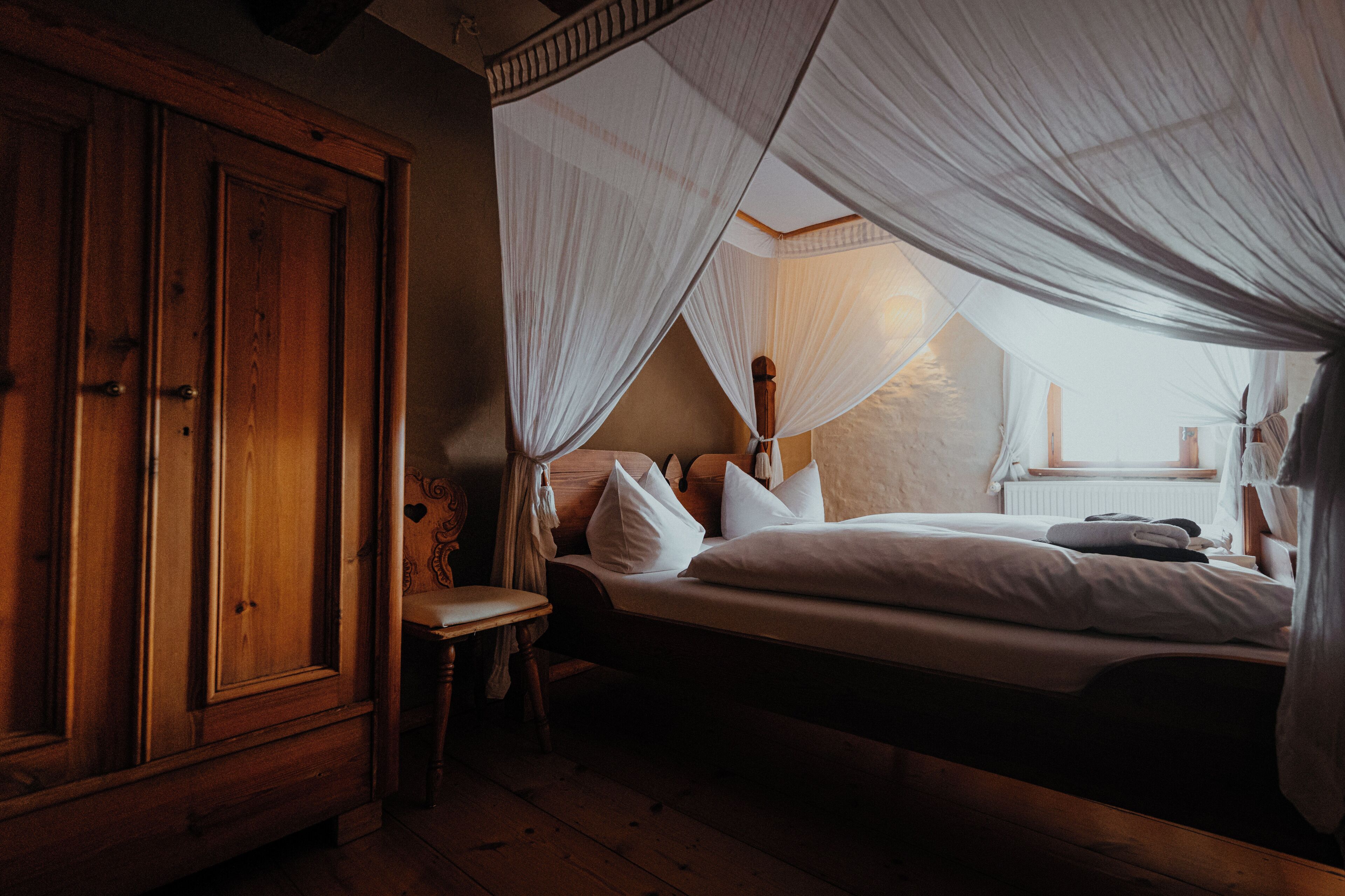 A bedroom with a wooden wardrobe, a bed with white bedding, and a canopy bed.