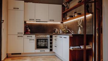 Cocina compacta con armarios blancos, horno empotrado y estante de madera con objetos decorativos.