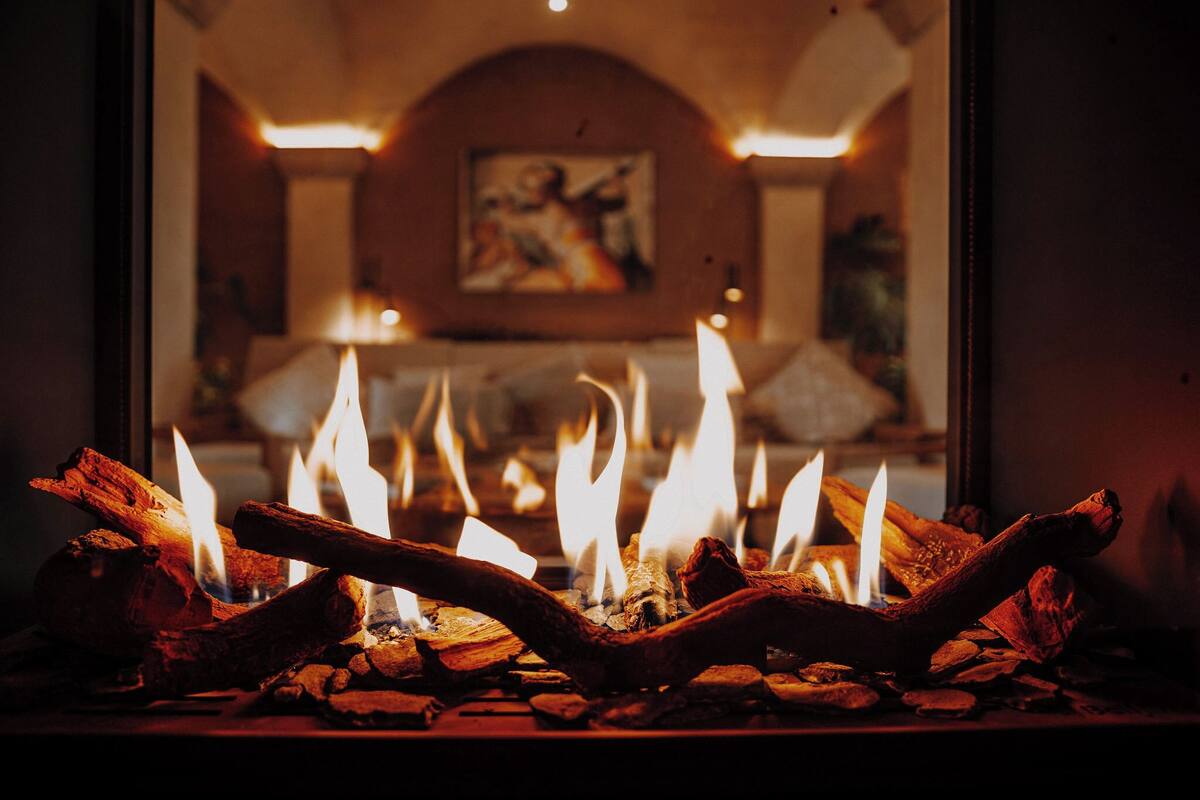 A fireplace with burning logs and flames, a painting on the wall, and a cozy interior setting.