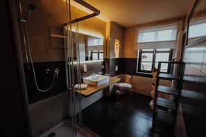 A modern bathroom with a glass shower enclosure, a wooden vanity, a white sink, and a toilet.