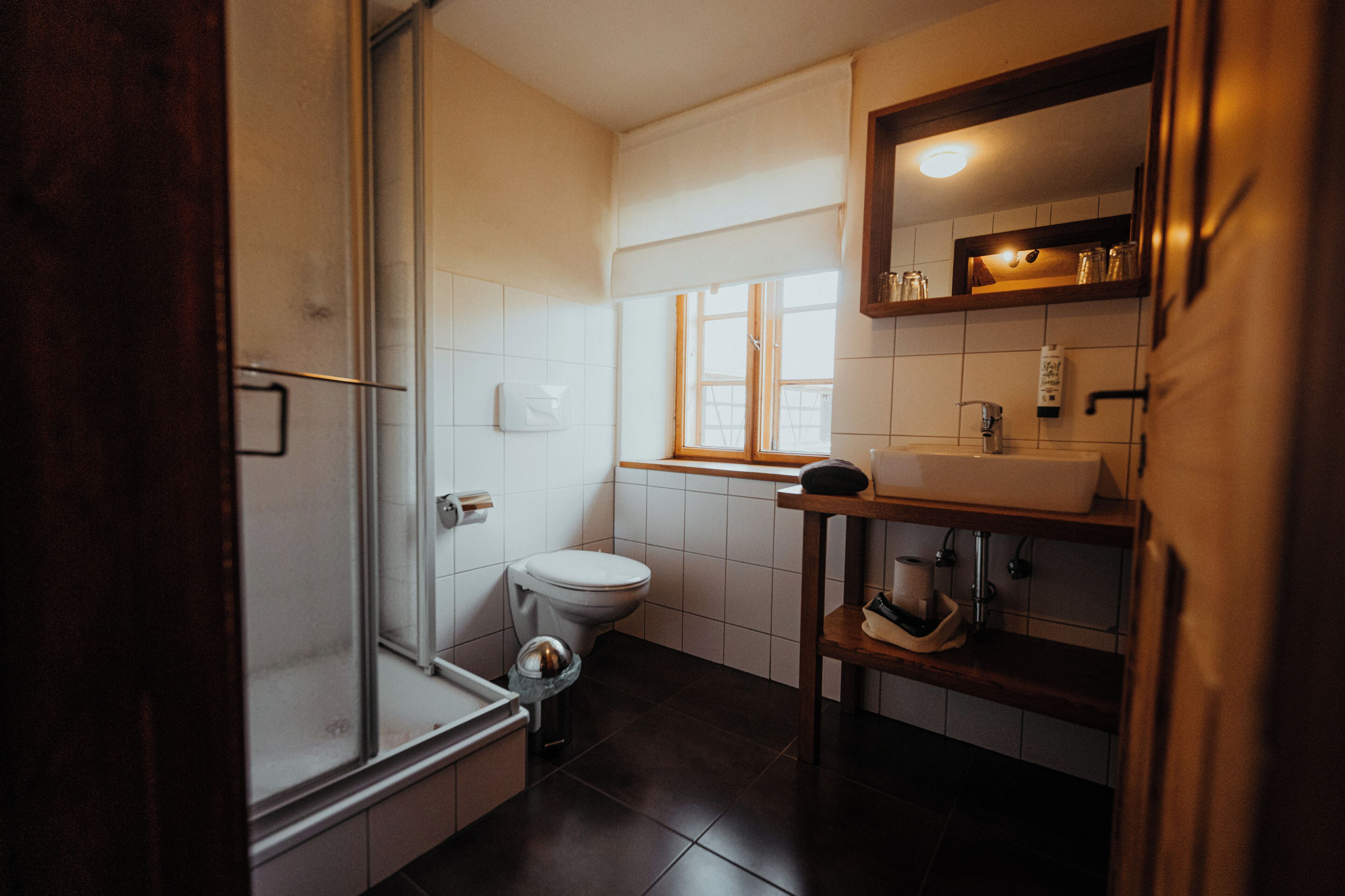 Uma casa de banho moderna com chuveiro de vidro, sanita branca e lavatório com espelho em cima.