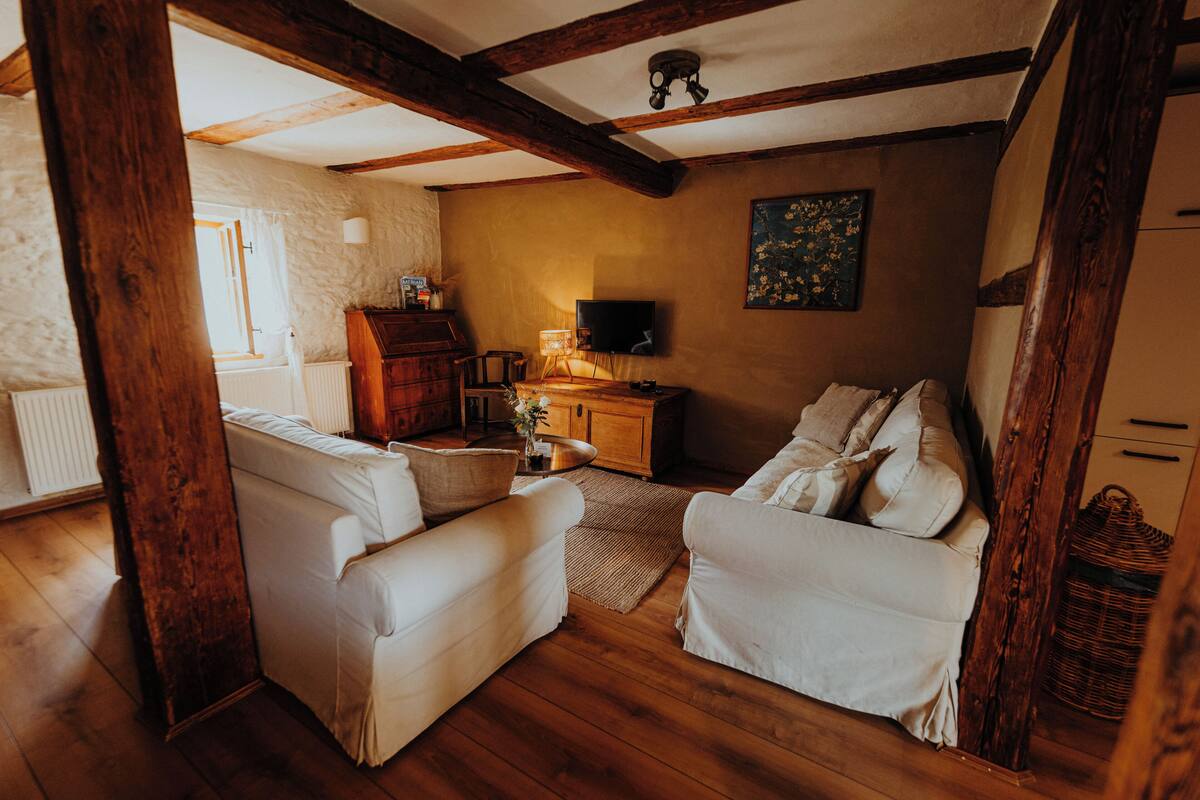 A cozy living room with wooden beams, white sofas, a wooden cabinet, a television, and a painting on the wall.