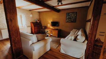 A cozy living room with wooden beams, white sofas, a wooden cabinet, a television, and a painting on the wall.