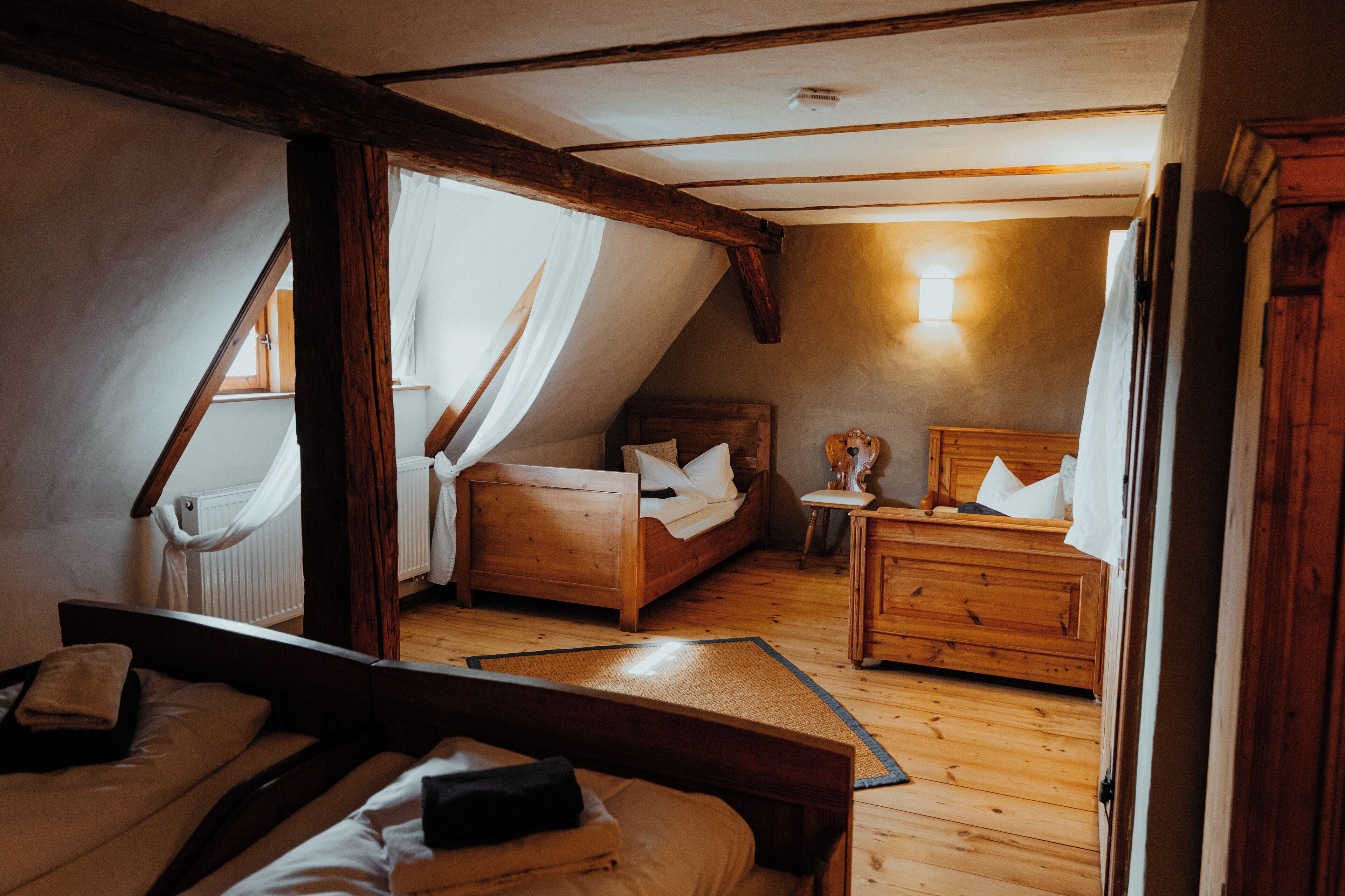 Un dormitorio acogedor en el ático con dos camas de madera, una mesita de noche pequeña y una lámpara.