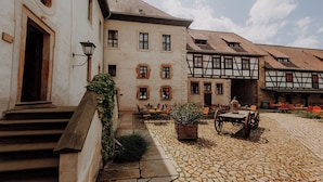 A courtyard with cobblestone flooring, a wooden bench, and a table with chairs. - Rittergut Positz GmbH (Oppurg)
