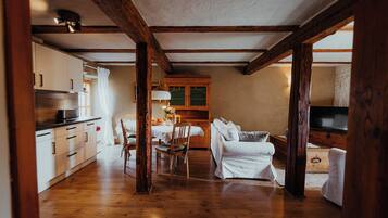 Uma sala de estar ampla com vigas de madeira, uma mesa de jantar com cadeiras, um sofá e uma televisão.