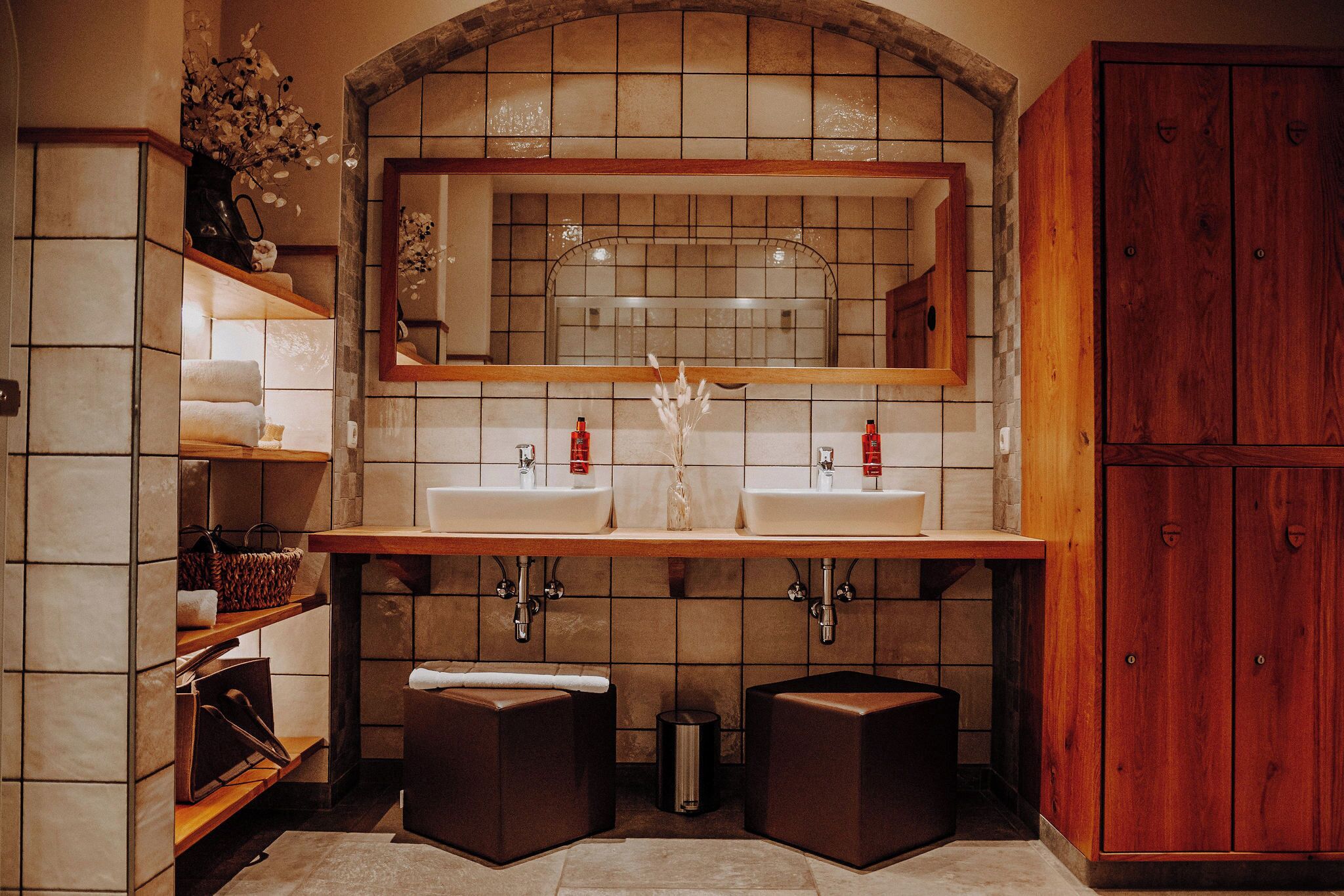 A bathroom with two sinks, a mirror, shelves with towels, and a wooden cabinet.