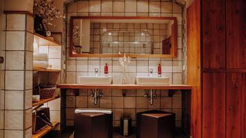 A bathroom with two sinks, a mirror, shelves with towels, and a wooden cabinet.