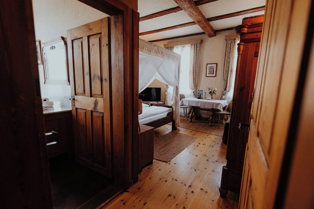 A wooden-floored bedroom with a bed, a bedside table, and a television.