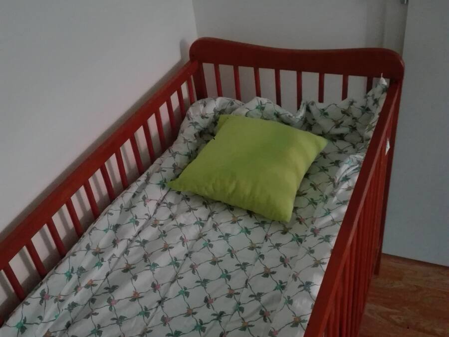 Een kleine kamer met een enkel bed, met een rode houten frame, een bloemenprint deken en een groen kussen.