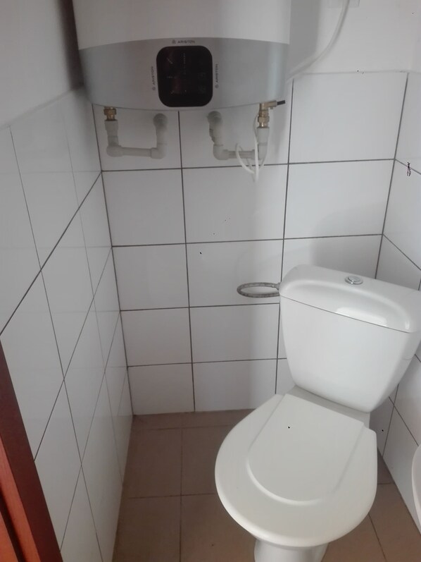 A small, tiled bathroom with a white toilet, a wall-mounted bidet, and a control panel above the toilet.