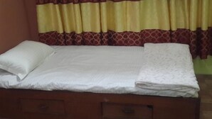 A single bed with white linens, a wooden headboard, and a patterned curtain. - Tamang Homestay (Dhulikhel)