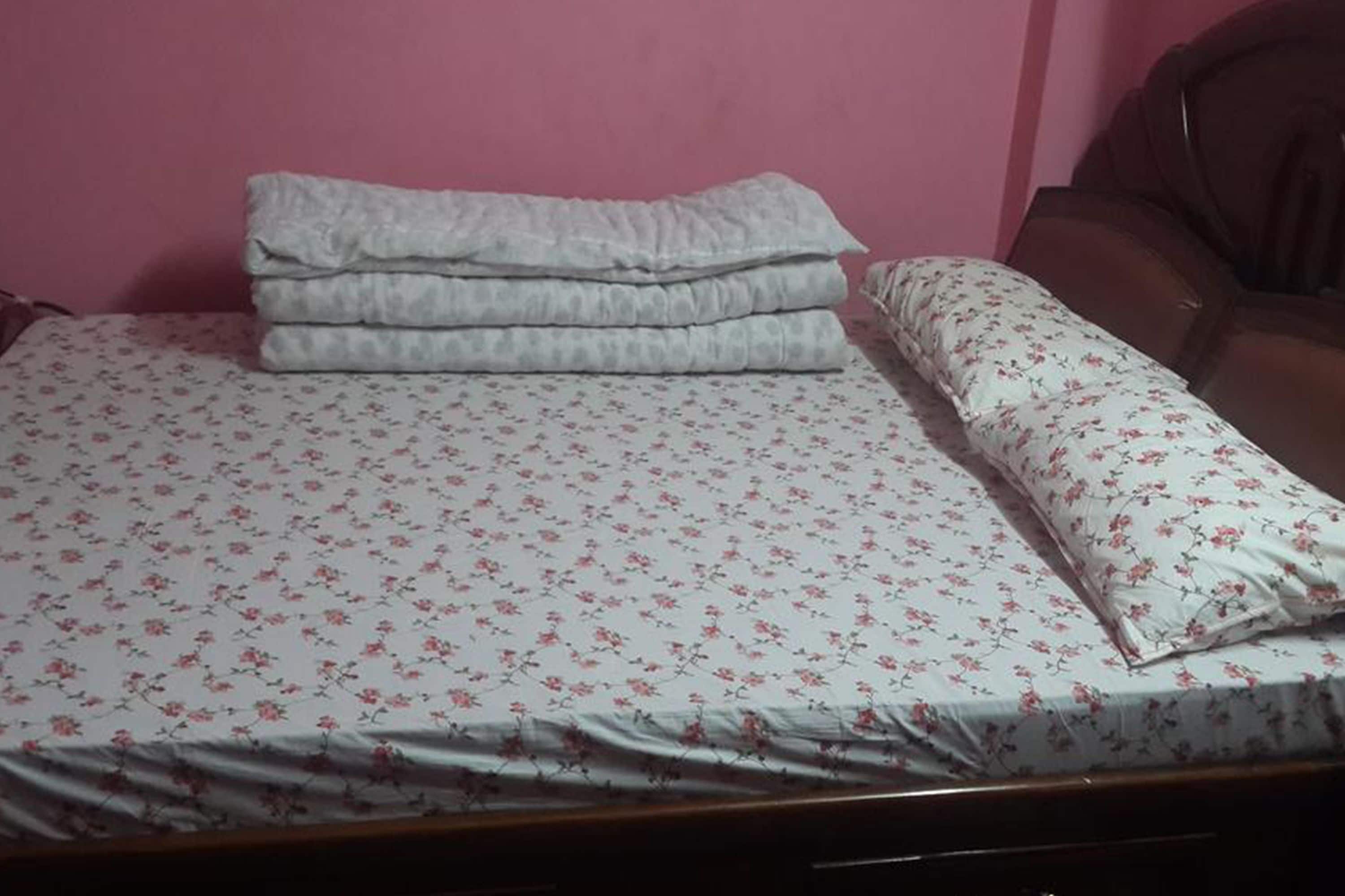 A bed with floral bedding and a stack of folded blankets.