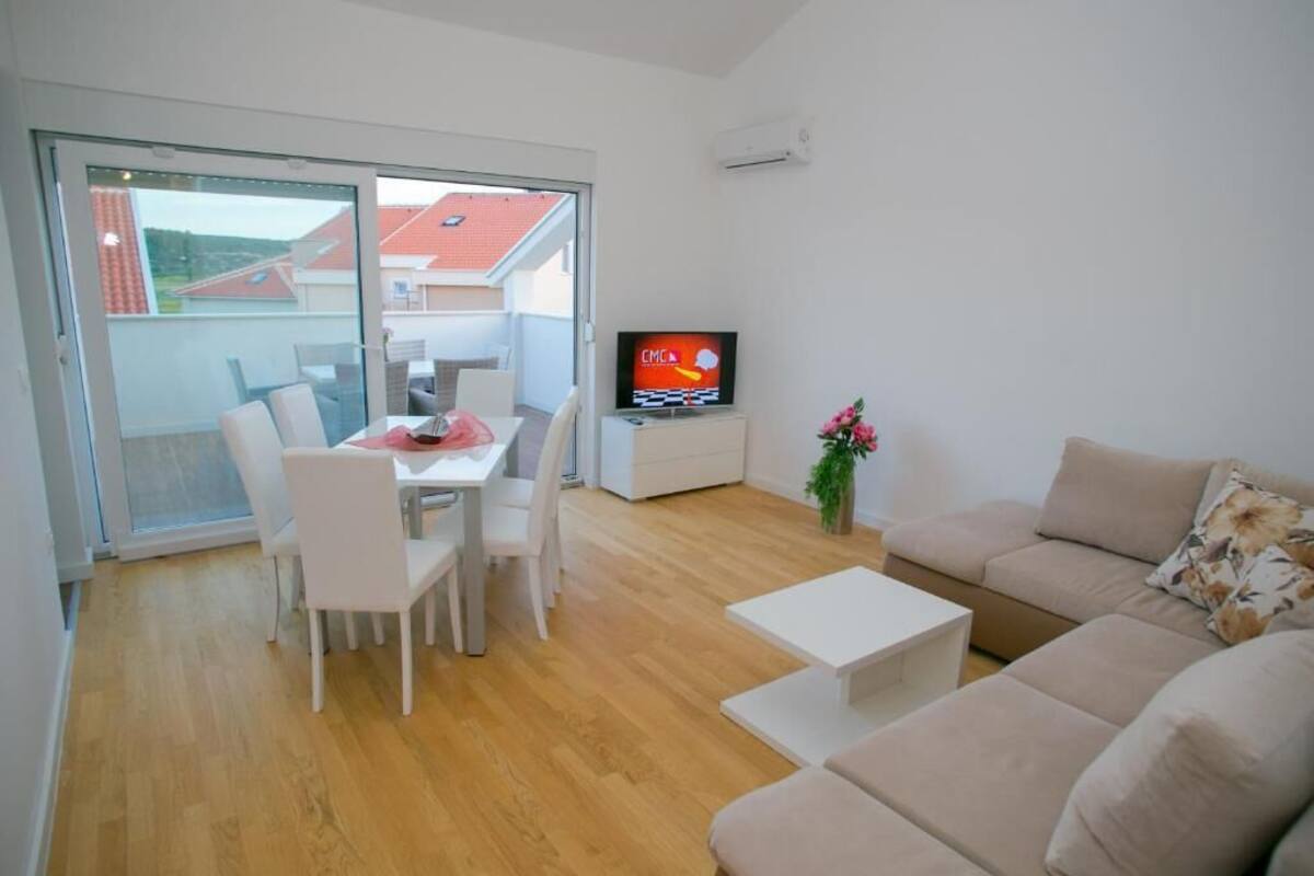 Ein modernes Wohnzimmer mit Essbereich, einer Couch, einem Fernseher und einer Glastür zum Balkon.