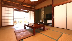 Et traditionelt japansk rum med tatamimåtter, et lavt træbord, siddehynder, skydedøre og et fjernsyn.