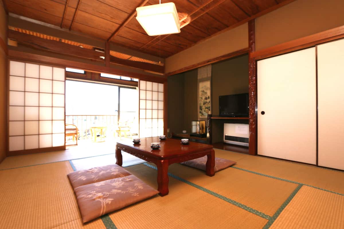 A traditional Japanese room with tatami flooring, a low wooden table, cushions, sliding doors, and a television.