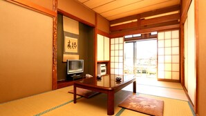 Et traditionelt japansk rum med tatami-gulv, et lavt træbord, et fjernsyn og skydedøre, der fører ud til en balkon.