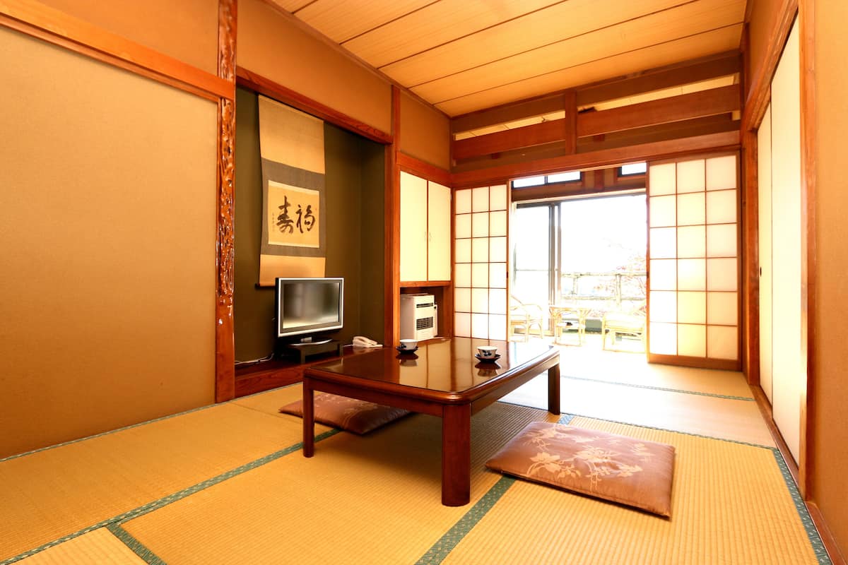 A traditional Japanese room with tatami flooring, a low wooden table, a television, and sliding doors leading to a balcony.