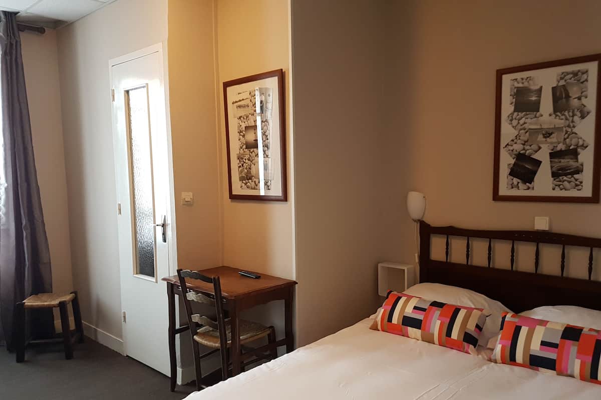 A hotel room with a bed, a desk, a chair, and a door.