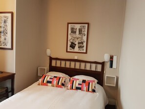 Un lit bien fait, agrémenté de coussins colorés, d’une tête de lit en bois et d’un tableau encadré au mur.