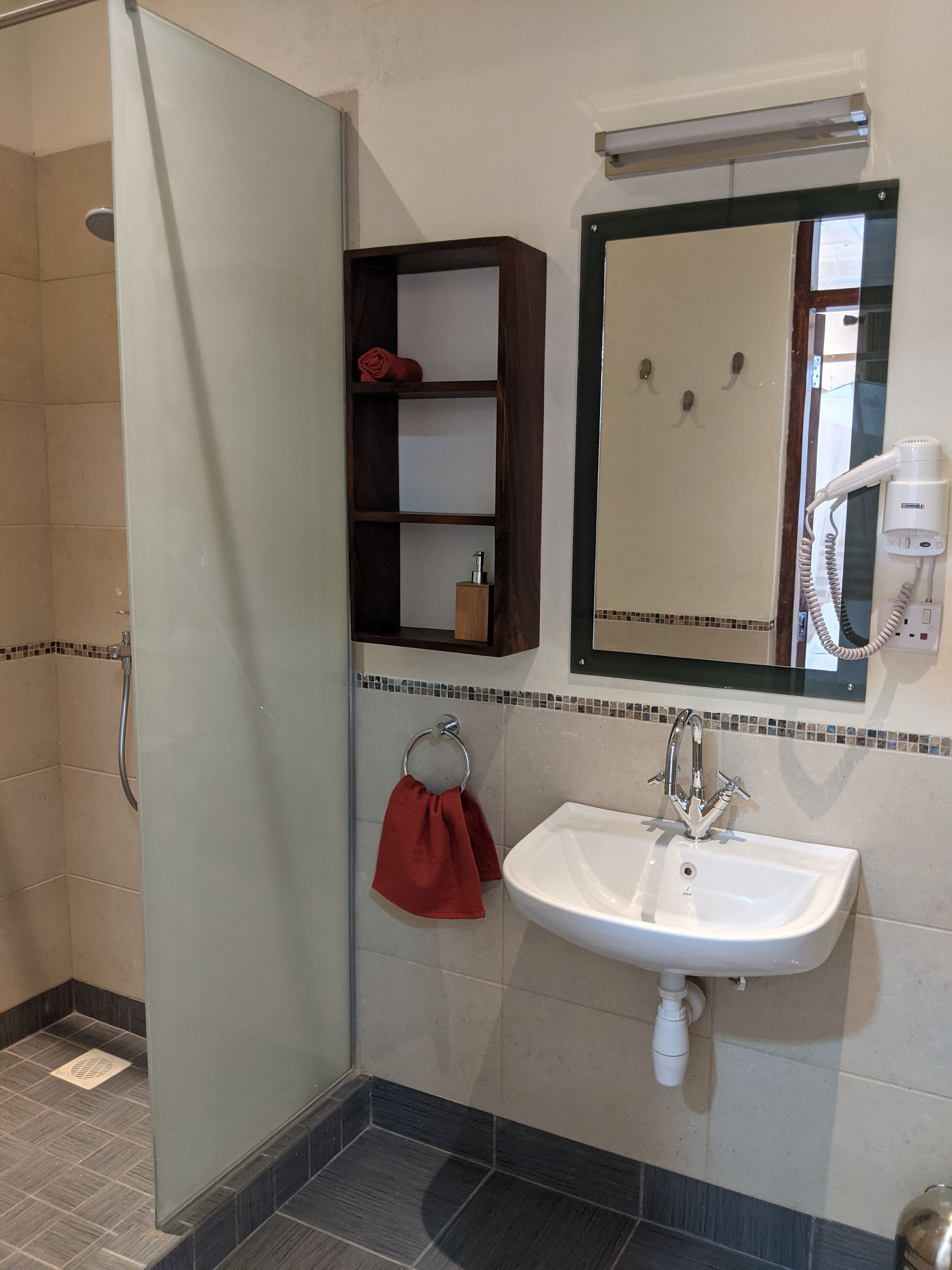 Een badkamer met een glazen douchedeur, een witte wastafel, een spiegel en een handdoekhouder met een rode handdoek.
