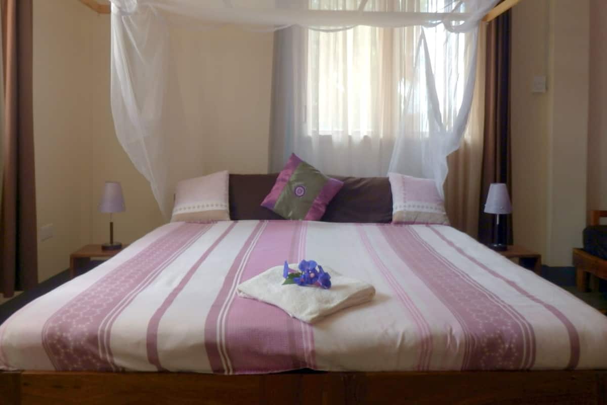 A bed with a canopy, pillows, a bedside table with a lamp, and a window with curtains.