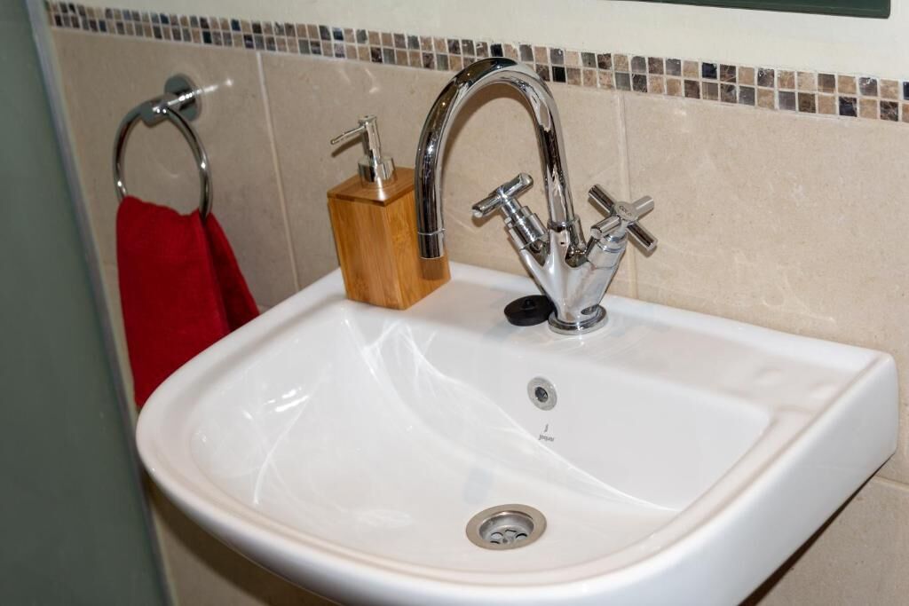 A white bathroom sink with a chrome faucet, a wooden soap dispenser, and a red towel on a metal ring.