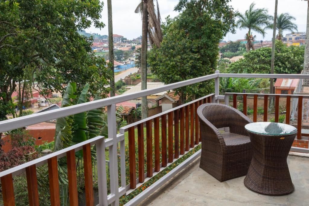 Varanda com cadeira de vime e mesa de vidro, com vista para área residencial com árvores e edifícios.