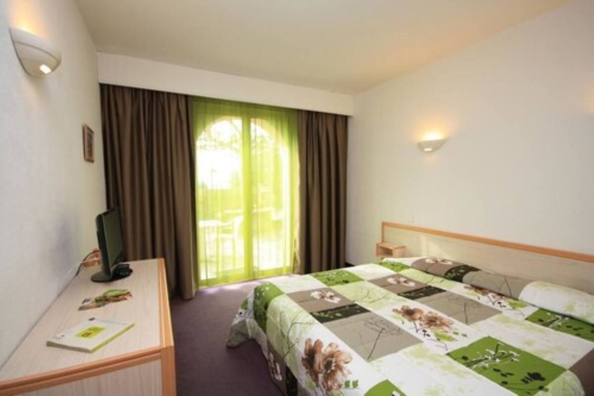 Habitación de hotel con cama, escritorio, silla y ventana con cortinas.