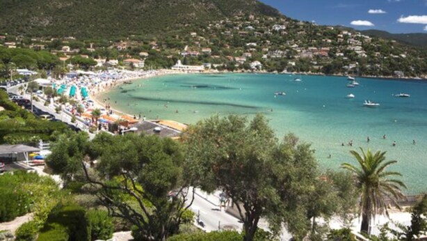 Un poble costaner amb una platja, embarcacions i un fons de muntanyes.
